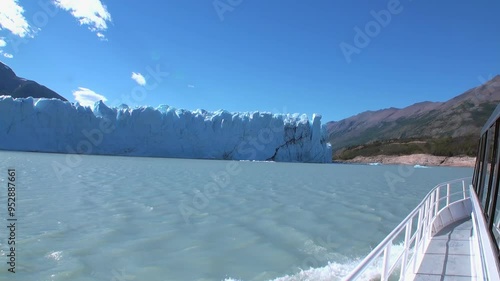 A boat navigates through the turquoise waters near towering glaciers in the Andes, Patagonia. The breathtaking landscape showcases the ice formations and rugged mountains under a clear blue sky. photo