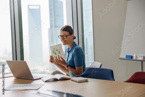 A focused professional woman is engaged with her book while skillfully working on a laptop in her sleek office