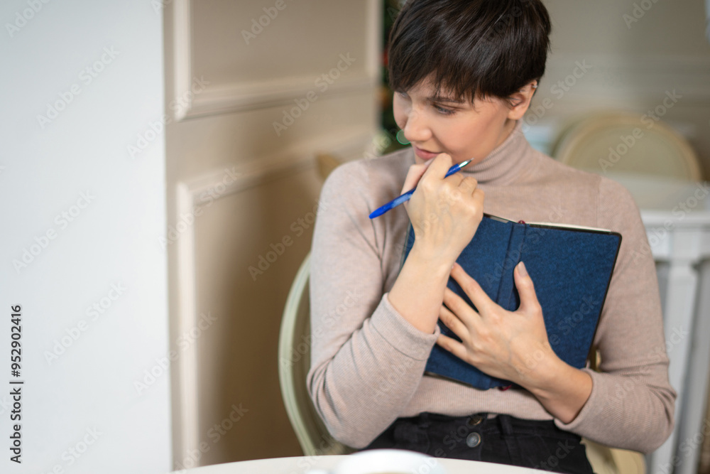 Attractive young woman with pen and notepad smiling while thinkking about new ideas in stylish cafe Attractive young woman with pen and notepad smiling while thinkking about new ideas in stylish cafe