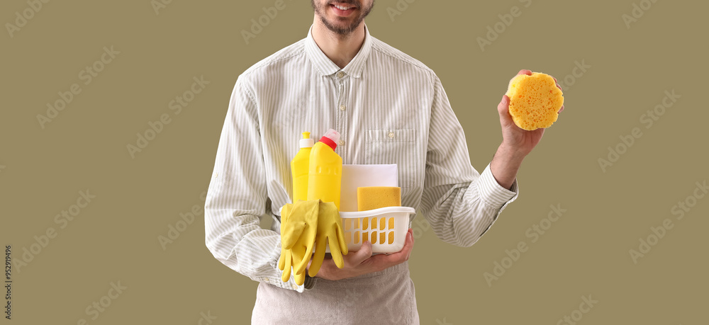 Young man with bucket of cleaning supplies on green background Young man with bucket of cleaning supplies on green background