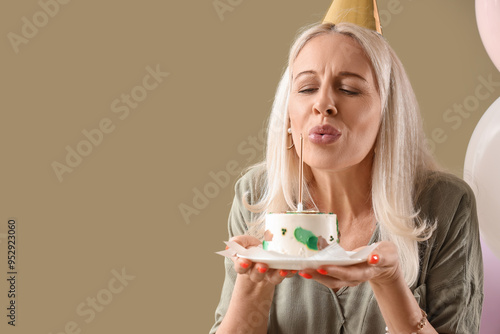 Mature woman with birthday cake making wish on green background, closeup