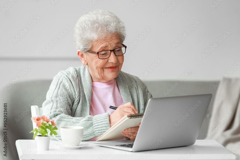 Senior woman with laptop writing in notebook at home Senior woman with laptop writing in notebook at home