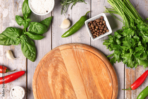 Composition with cutting board, fresh herbs and spices on light wooden background photo