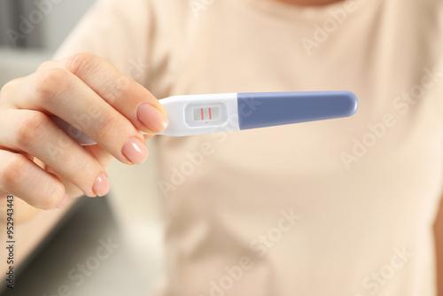 Woman holding positive pregnancy test indoors, closeup view