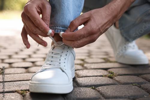 Man tying shoelace of white sneaker outdoors, closeup