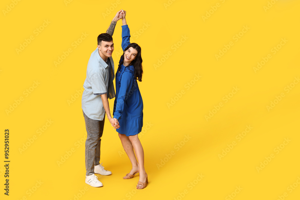 Fototapeta premium Happy young couple dancing on yellow background