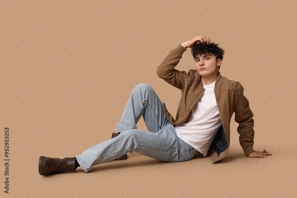 Handsome young man in stylish clothes sitting against brown background Handsome young man in stylish clothes sitting against brown background