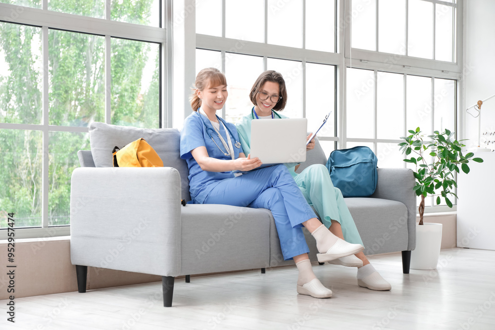 Female medical interns using laptop on sofa in clinic Female medical interns using laptop on sofa in clinic