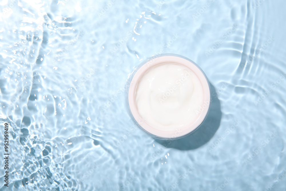 Cosmetic product. Jar with cream in water on light blue background, top view. Space for text Cosmetic product. Jar with cream in water on light blue background, top view. Space for text