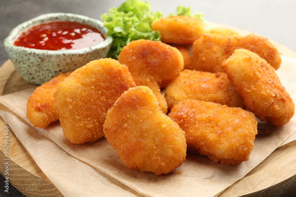 Board with hot chili sauce, lettuce and nuggets on table, closeup Board with hot chili sauce, lettuce and nuggets on table, closeup