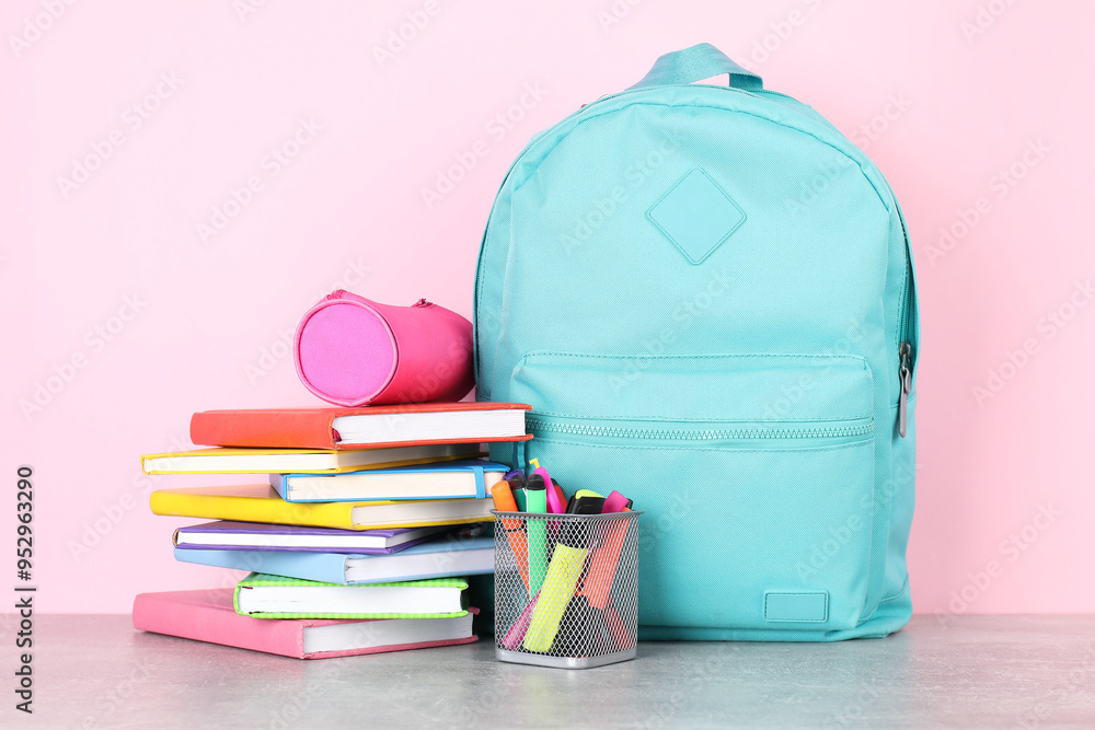 Backpack with different school stationery on light grey table against pink background Backpack with different school stationery on light grey table against pink background