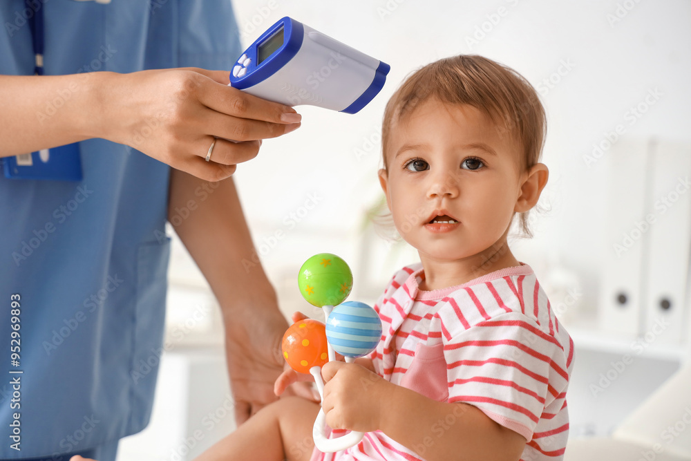 Female pediatrician measuring temperature of cute little baby with rattle in clinic Female pediatrician measuring temperature of cute little baby with rattle in clinic