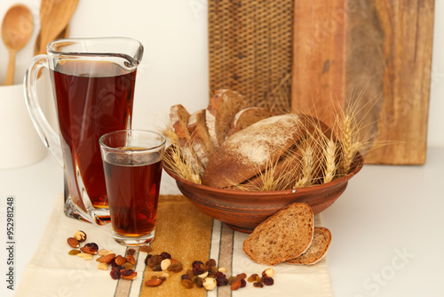 Jug and glass of tasty kvass with bread on table in kitchen photo