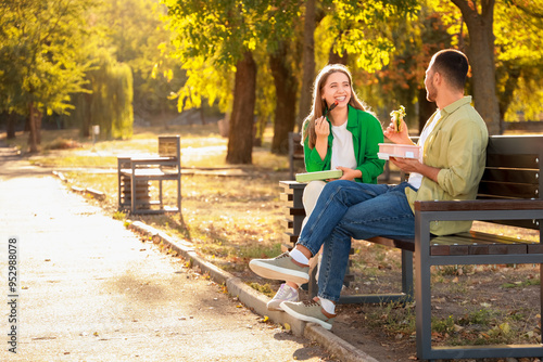Young couple having lunch on bench in park