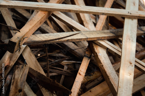 A pile of wood with many pieces of wood scattered around. The wood is brown and has a rough texture. The pile of wood appears to be from a construction site or a woodworking project