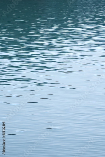 A serene view of calm water with gentle ripples, reflecting a soft blue hue. The surface appears smooth and tranquil, creating a peaceful atmosphere.