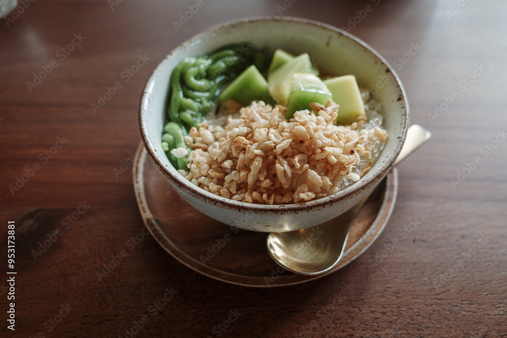 A close-up view of a refreshing traditional Thai dessert featuring a mix of diced taro, green pandan noodles, and melon pieces served in a bowl with coconut milk and crushed ice. A close-up view of a refreshing traditional Thai dessert featuring a mix of diced taro, green pandan noodles, and melon pieces served in a bowl with coconut milk and crushed ice.