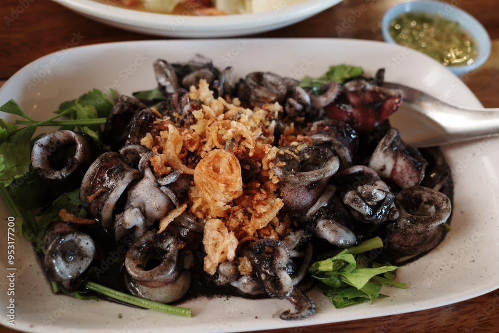 A close-up shot of a delectable dish featuring stir-fried squid cooked in its own black ink. A close-up shot of a delectable dish featuring stir-fried squid cooked in its own black ink.