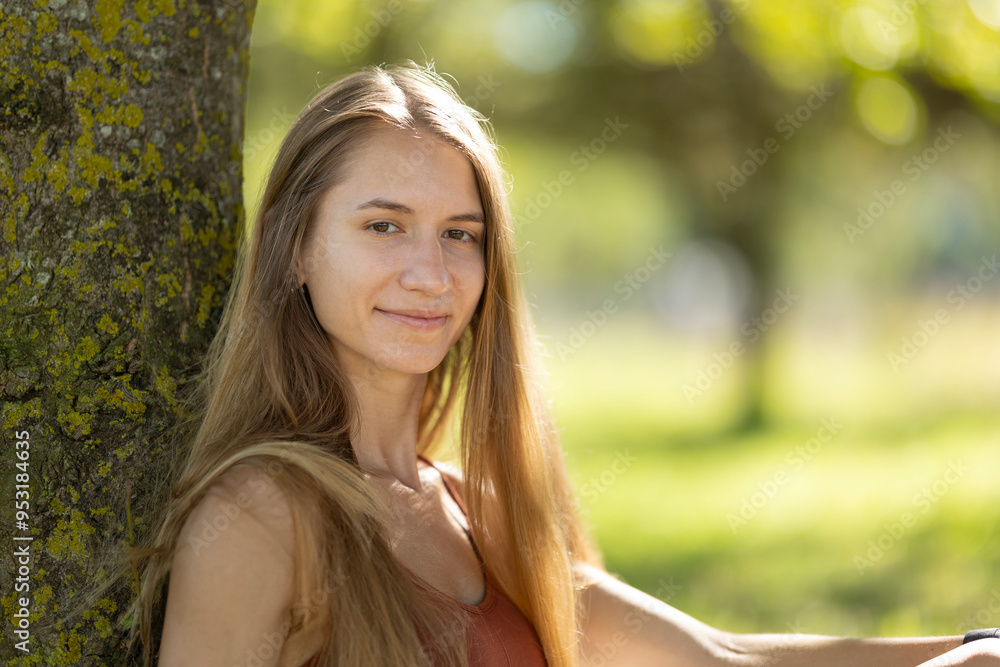Young woman relaxing in park leaning on tree Young woman relaxing in park leaning on tree
