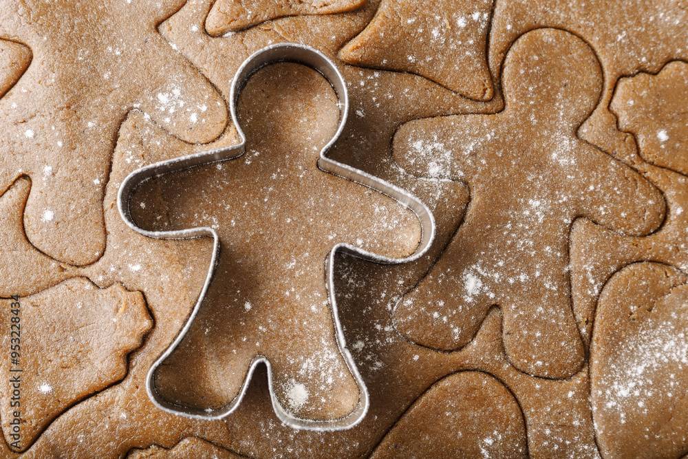Cooking ginger cookies, Christmas and New Year traditional cookies in shape of gingerbread man, raw rolled out dough with cut out dough figures, closeup texture, top view, metal pastry cutter on dough