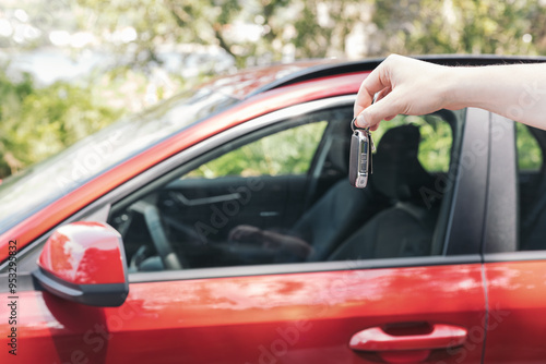 A close-up of a hand holding a car key next to a red vehicle. Concept of vehicle ownership, car rental, or a new car purchase.