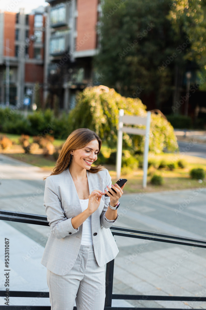 Young professional woman dressed in business attire smiles while texting on her smartphone in a vibrant urban setting during daylight Young professional woman dressed in business attire smiles while texting on her smartphone in a vibrant urban setting during daylight