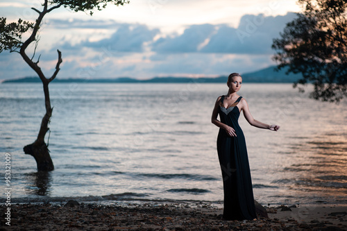 Beauty and nature. Fairy and sensual portrait of pretty young woman wearing long black dress against dramatic sky and sea view photo