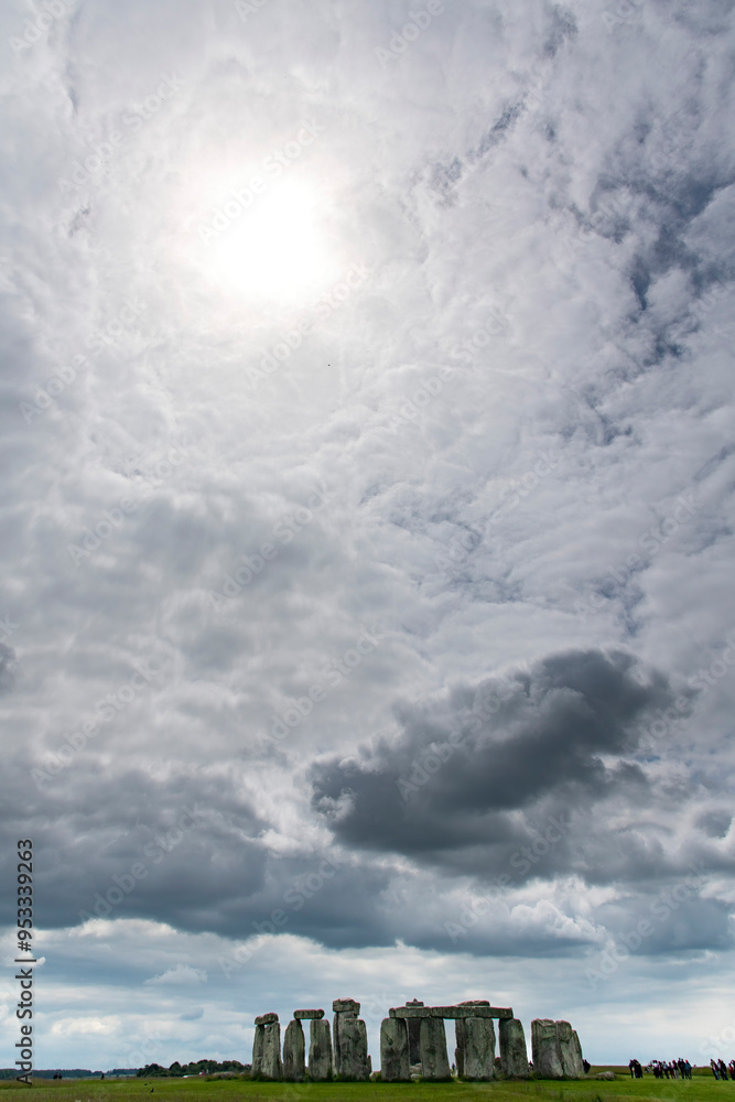 Dramatic cloudscape with sun shining bright through clouds above Stonehenge prehistoric structure on Salisbury Plain, Wiltshire, England with vertical sarsen standing stones and smaller Dramatic cloudscape with sun shining bright through clouds above Stonehenge prehistoric structure on Salisbury Plain, Wiltshire, England with vertical sarsen standing stones and smaller