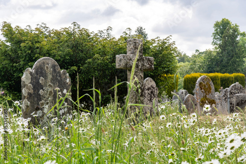 Graveyard with headstones of the St Michael the Archangel Church in Chagford, UK between a field of blooming white lawn daisies photo