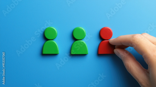 Hand selecting a red figure among green figures on blue background. Concept of individuality, uniqueness, and selection. photo