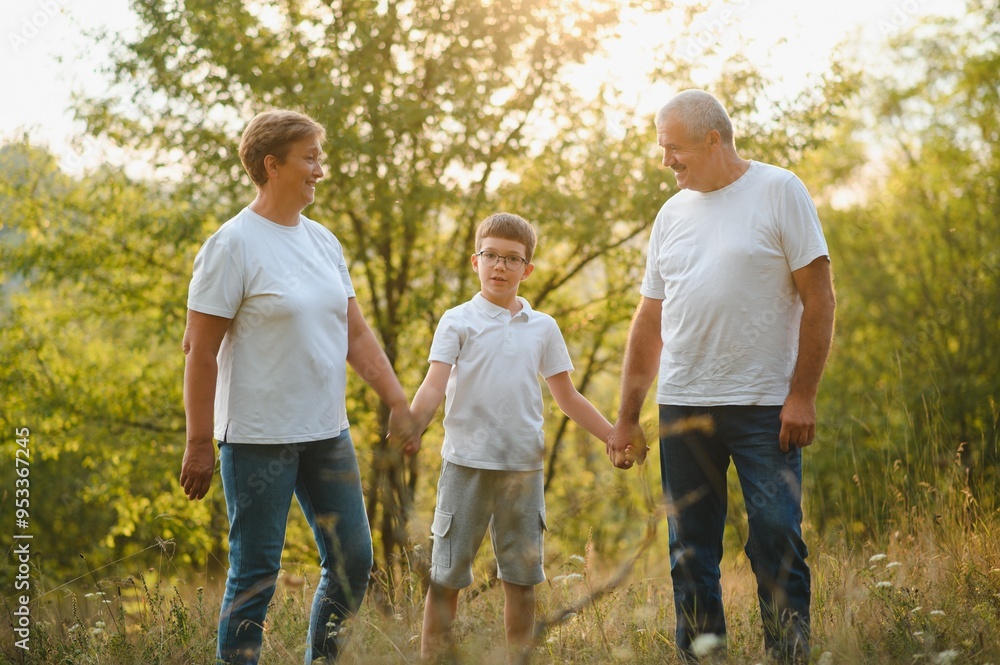 Grandson, grandfather and grandmother sitting on grass having fun outdoors in park at sunset