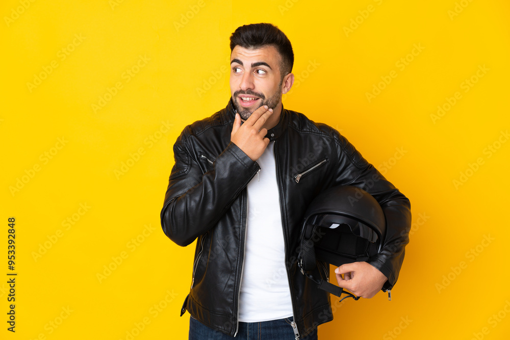 Caucasian man with a motorcycle helmet over isolated yellow background looking up while smiling Caucasian man with a motorcycle helmet over isolated yellow background looking up while smiling