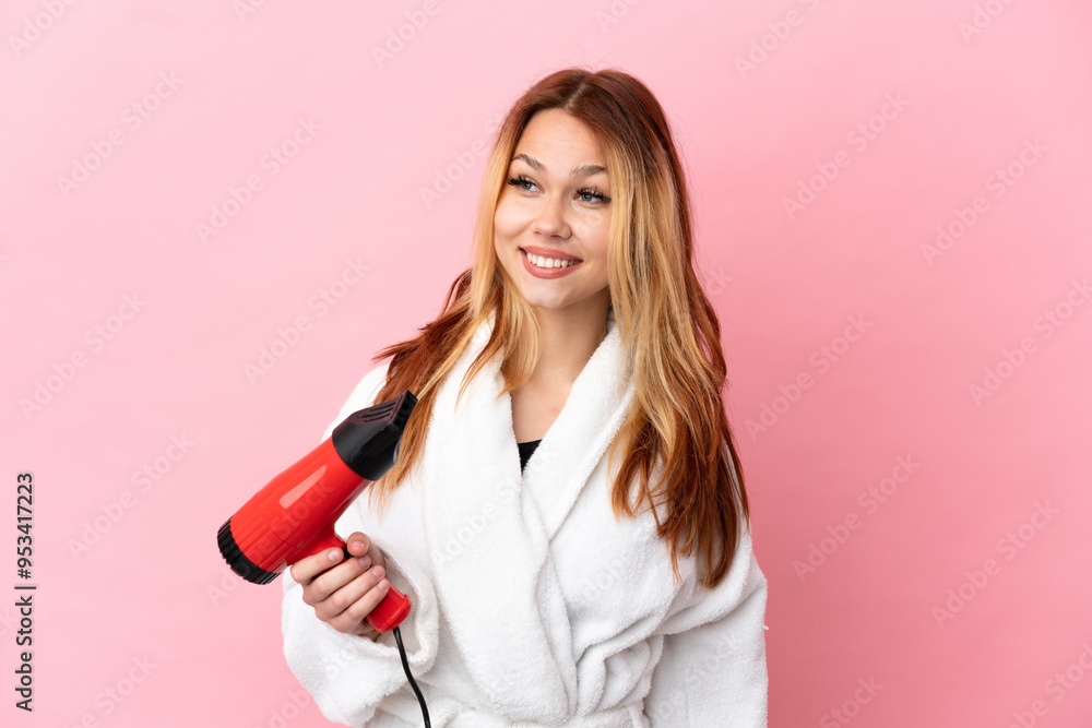 Teenager blonde girl holding a hairdryer over isolated pink background looking to the side and smiling Teenager blonde girl holding a hairdryer over isolated pink background looking to the side and smiling