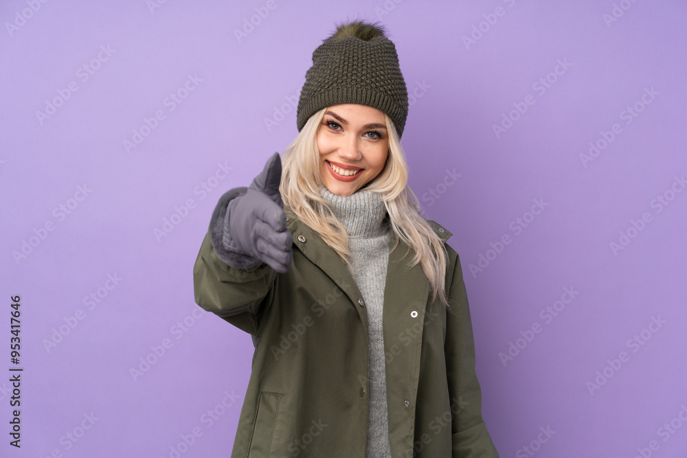 Teenager blonde girl with winter hat over isolated purple background shaking hands for closing a good deal Teenager blonde girl with winter hat over isolated purple background shaking hands for closing a good deal