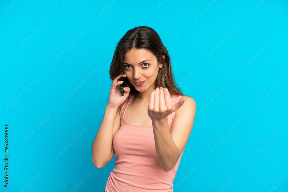 Young caucasian woman using mobile phone isolated on blue background inviting to come with hand. Happy that you came Young caucasian woman using mobile phone isolated on blue background inviting to come with hand. Happy that you came