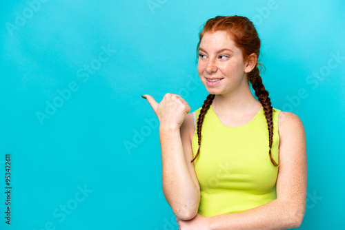 Young reddish woman isolated on blue background pointing to the side to present a product