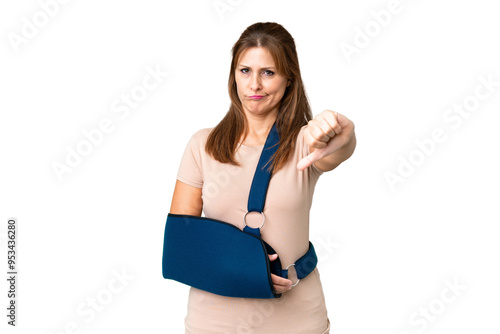 Middle age with broken arm and wearing a sling over isolated background showing thumb down with negative expression