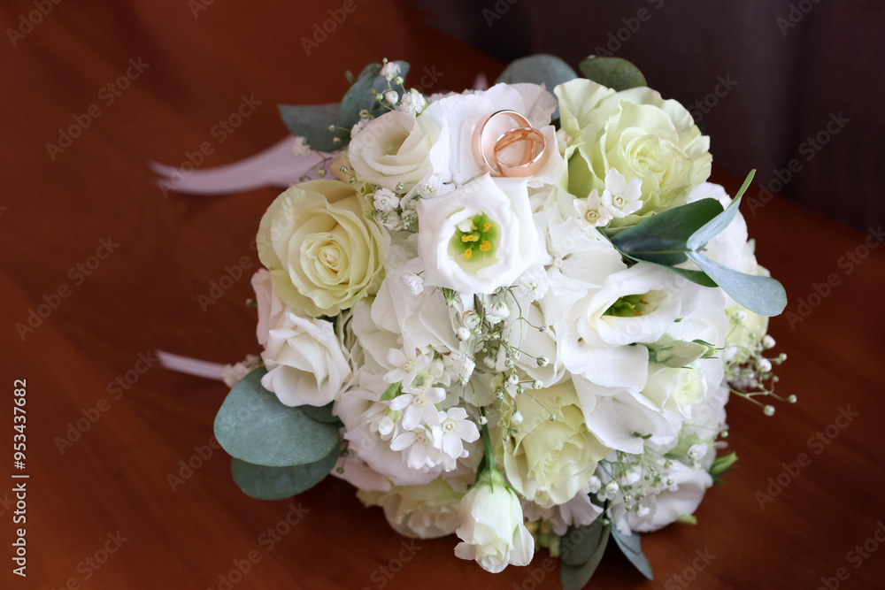 On the table is a wedding bouquet of white roses and two gold wedding rings. On the table is a wedding bouquet of white roses and two gold wedding rings.