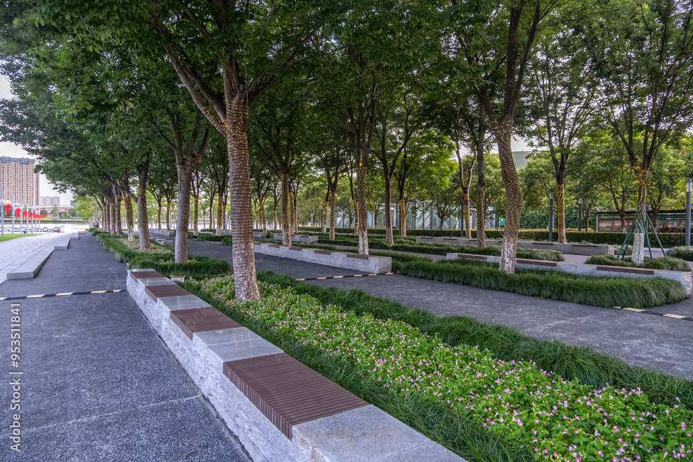 a beautifully landscaped urban park with a long, straight pathway lined by rows of tall trees, bordered by low stone seats and trimmed hedges. An inviting and clean parkland with outdoor seating space a beautifully landscaped urban park with a long, straight pathway lined by rows of tall trees, bordered by low stone seats and trimmed hedges. An inviting and clean parkland with outdoor seating space