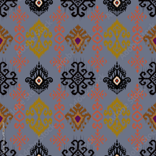 This image showcases an intricate Ikat pattern featuring stylized shapes in black, orange, and gold on a gray background, forming a repetitive, symmetrical design.
