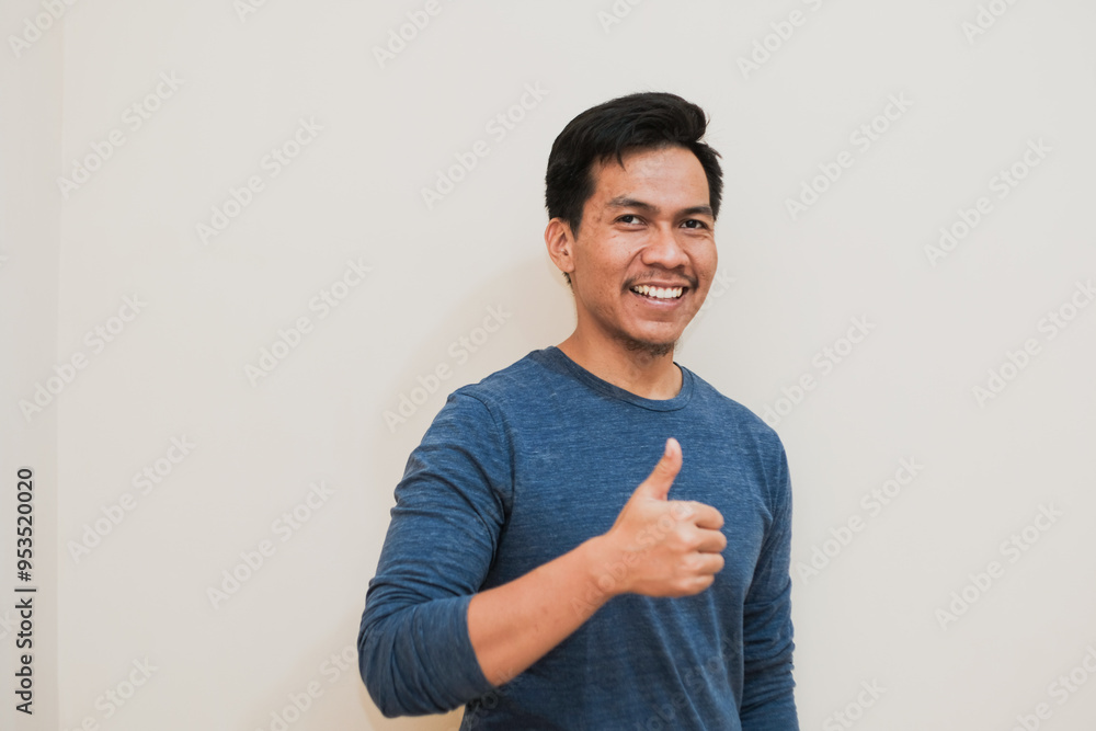 Adult Southeast Asian man smiling at the camera while giving thumbs up, positive emotion, copy space. Adult Southeast Asian man smiling at the camera while giving thumbs up, positive emotion, copy space.