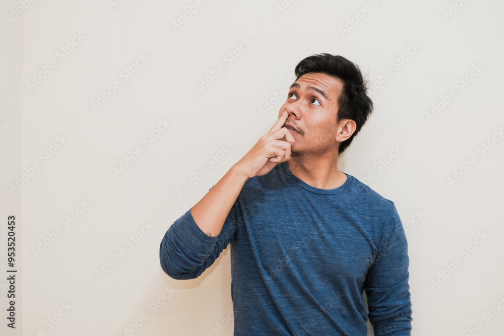 Adult Southeast Asian man is picking his nose isolated on cream background, fooling around, showing his bad manners. Adult Southeast Asian man is picking his nose isolated on cream background, fooling around, showing his bad manners.