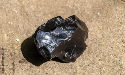 A piece of black obsidian on concrete. Black obsidian on the ground