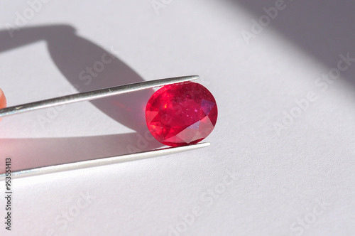 Lead glass filled natural ruby gemstone in tweezers. Heated, treated, affordable red gemstone. Mass market ruby gemstone mined in Madagascar, faceted in Thailand. Bright red colored gemstone setting.
 photo