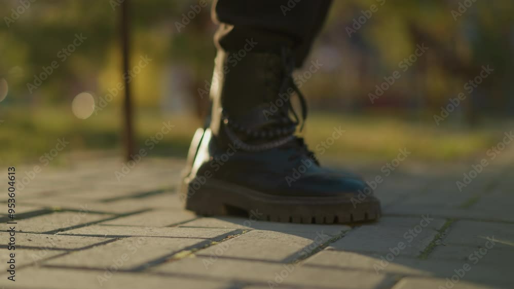 A close-up shot of black boots stepping on a paved path in a sunlit park. The focus is on the boots, showing the details of the laces and sturdy soles. The background is softly blurred A close-up shot of black boots stepping on a paved path in a sunlit park. The focus is on the boots, showing the details of the laces and sturdy soles. The background is softly blurred