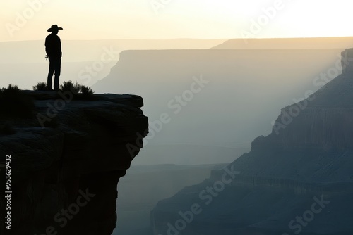 A lone figure stands on a cliff at sunset, overlooking a vast canyon landscape.