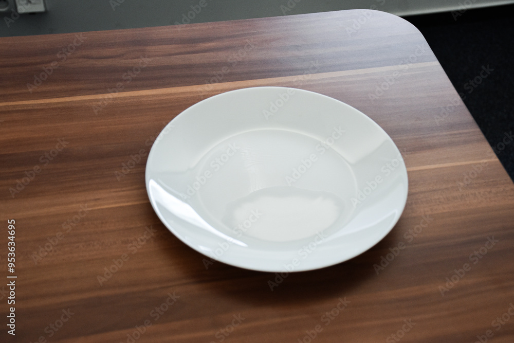 White ceramic plate on a wooden surface. Minimalist table setting, perfect for modern dining or kitchen decor with a simple and clean aesthetic White ceramic plate on a wooden surface. Minimalist table setting, perfect for modern dining or kitchen decor with a simple and clean aesthetic
