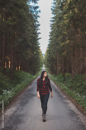 Wallpaper Mural Young woman in a red plaid shirt walking down a peaceful, tree-lined forest road, embracing the tranquility and beauty of nature, symbolizing freedom and a journey of self-discovery Torontodigital.ca
