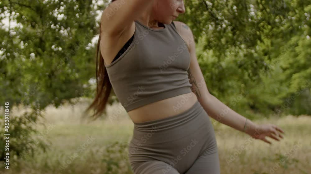 A young woman wearing fitness attire dances in a sunny park. She is enjoying the summer weather while getting exercise. A young woman wearing fitness attire dances in a sunny park. She is enjoying the summer weather while getting exercise.