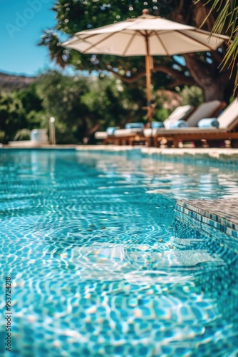 Swimming pool at a resort. Clear blue water, lounge chairs for relaxation, umbrella providing shade.